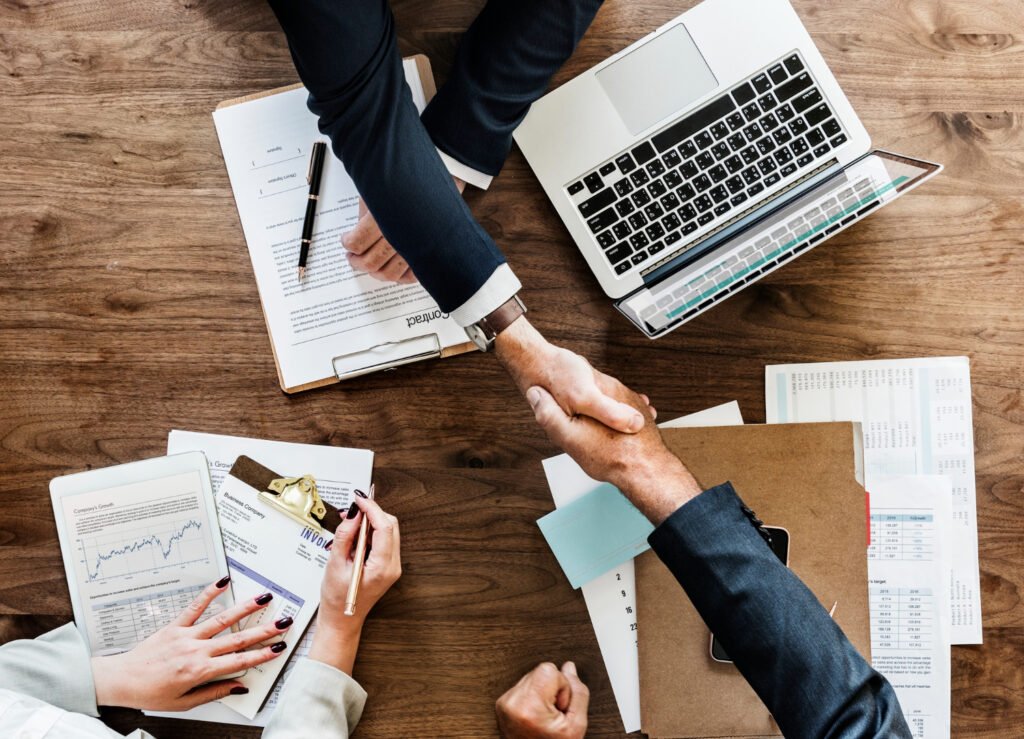 changemanagement Zwei Personen schütteln sich die Hände über Papiere auf einem Tisch